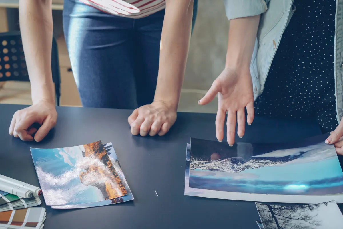 Two people at a dark table comparing large landscape photo prints and a colour swatch book