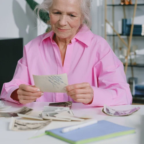 A woman in a pink shirt holding an old photograph at a table covered in vintage prints