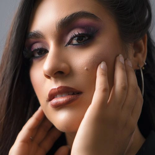 A close-up portrait of a woman wearing a purple smoky eye and a warm brown lip
